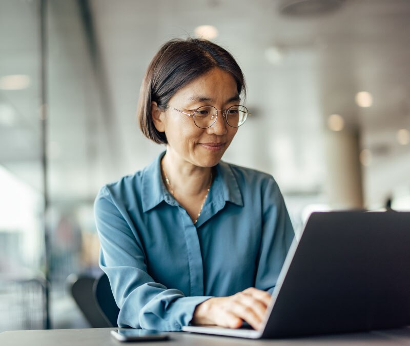 A woman sits at her laptop and adds login credentials to her password manager.