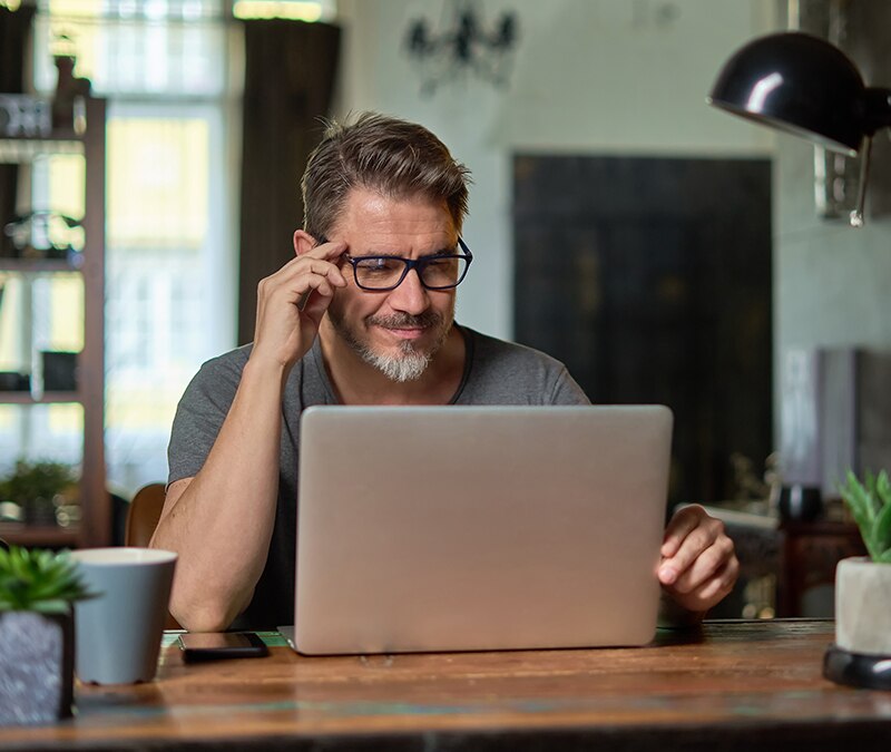 A man with glasses working on a laptop at a table.